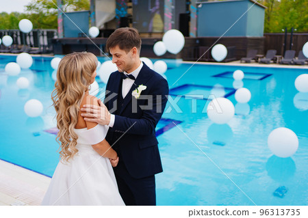 bride and groom in classic clothes by the pool decorated with white balloons. bride and groom in classic clothes by the pool decorated with white balloons. 96313735