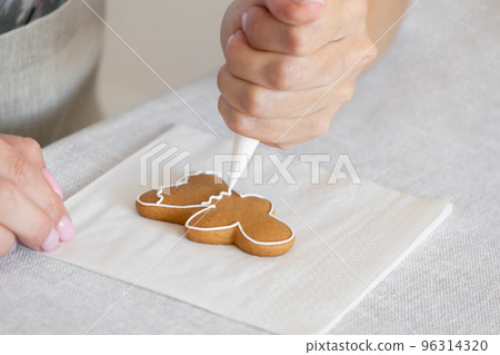 Women's hands decorate sugar icing homemade traditional New Year's cookies snowflake gingerbread man 96314320