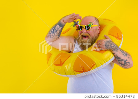 Fat happy man with wig in head is ready to swim with a donut lifesaver Fat happy man with wig in head is ready to swim with a donut lifesaver 96314478