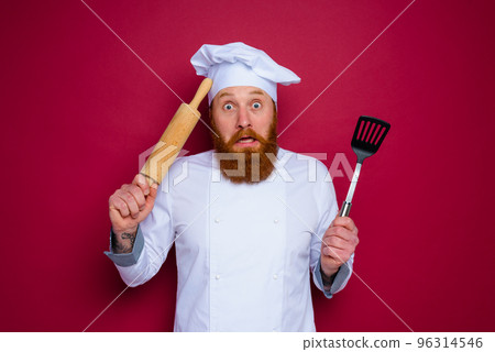 confused chef with beard and red apron chef holds wooden rolling pin 96314546