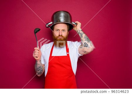 unhappy chef with beard and red apron plays with pot 96314623