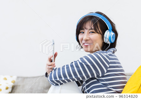 Woman sitting on sofa and listening to music with headphones Woman sitting on sofa and listening to music with headphones 96314820