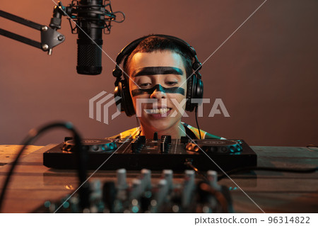 Musical artist acting funky looking at mixer, being focused on control buttons at dj turntables over background. Looking closely at audio equipment to mix techno music, stereo instrument. 96314822