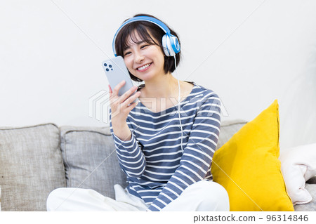 Woman sitting on sofa and listening to music with headphones 96314846