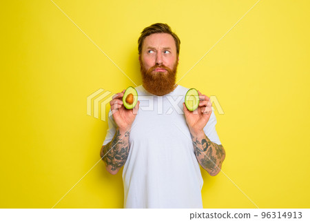 Doubter man with beard and tattoos holds an avocado 96314913