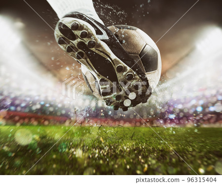 Football scene at night match with close up of a soccer shoe hitting the ball with power Football scene at night match with close up of a soccer shoe hitting the ball with power 96315404