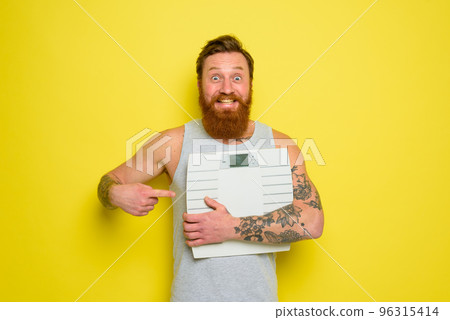 Amazed man with beard and tattoos holds an electronic balance Amazed man with beard and tattoos holds an electronic balance 96315414