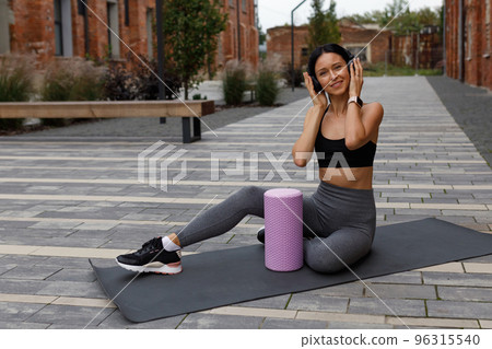 Portrait of cheerful fitness woman in headphones listening music while sitting on yoga mat outdoors Portrait of cheerful fitness woman in headphones listening music while sitting on yoga mat outdoors 96315540