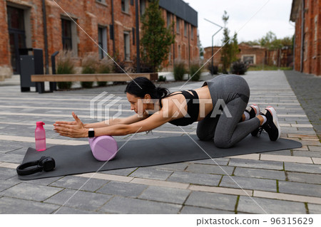 Adult athletic woman in sportswear exercising with foam roller on the yoga mat outdoor 96315629