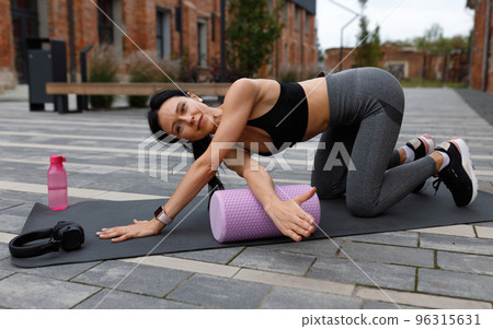 Strong woman doing fitness exercises outdoor, using fascia massage roller 96315631