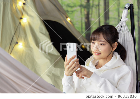 Home time: A woman using a smartphone while relaxing in a hammock 96315836