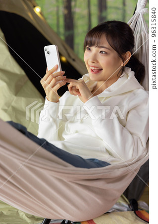 Home time: A woman using a smartphone while relaxing in a hammock 96315840