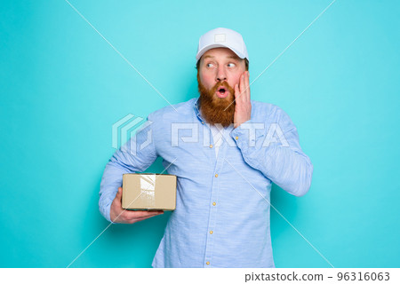 Courier with carton box in hand is surprised about something Courier with carton box in hand is surprised about something 96316063