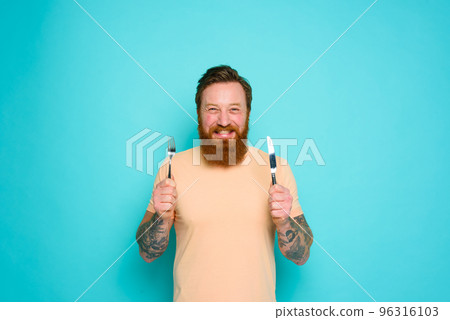 Happy man with tattoos is ready to eat with cutlery in hand Happy man with tattoos is ready to eat with cutlery in hand 96316103