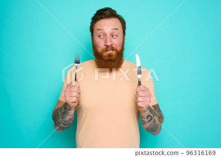 Happy man with tattoos is ready to eat with cutlery in hand 96316169