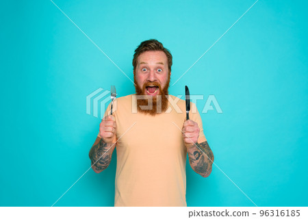 Happy man with tattoos is ready to eat with cutlery in hand Happy man with tattoos is ready to eat with cutlery in hand 96316185