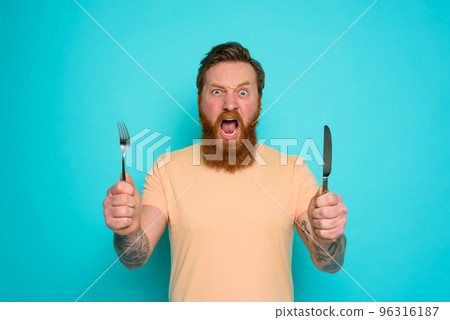 Hungry man with tattoos is ready to eat with cutlery in hand Hungry man with tattoos is ready to eat with cutlery in hand 96316187