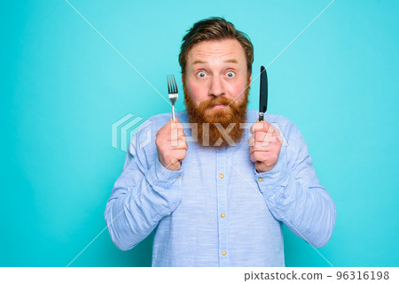 Man with tattoos is ready to eat with cutlery in hand Man with tattoos is ready to eat with cutlery in hand 96316198