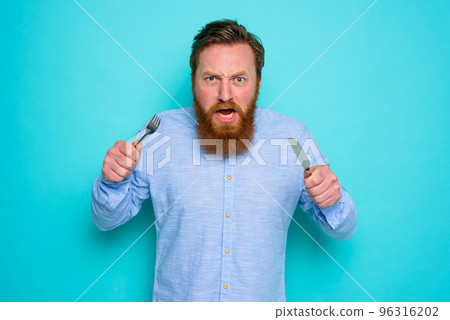 Hungry man with tattoos is ready to eat with cutlery in hand Hungry man with tattoos is ready to eat with cutlery in hand 96316202