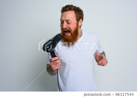 Happy man with beard use hair dryer as microphone and dances Happy man with beard use hair dryer as microphone and dances 96317543