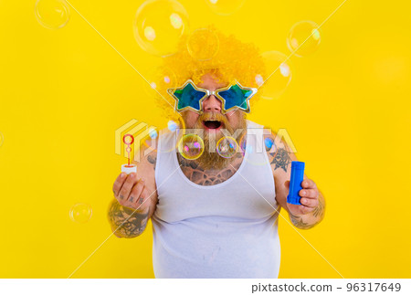 Amazed man with yellow wig in head play with bubbles soap 96317649