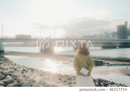 Photo of a young woman standing while reading on the riverbed Photo of a young woman standing while reading on the riverbed 96317754