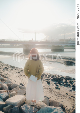 Photo of a young woman standing while reading on the riverbed 96317755