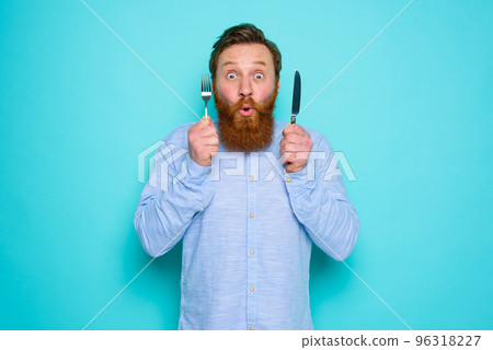 Shocked man with tattoos is ready to eat something with cutlery in hand 96318227