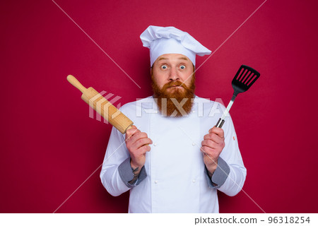doubter chef with beard and red apron chef holds wooden rolling pin 96318254