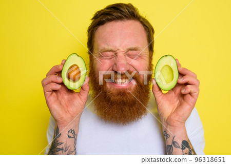 Happy man with beard and tattoos holds an avocado 96318651