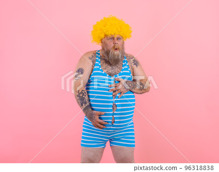 Happy man with yellow wig and swimsuit has stomachache 96318838