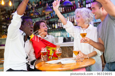 Cheerful international sport football fans waving Spanish flag and drinking beer in the sport bar Cheerful international sport football fans waving Spanish flag and drinking beer in the sport bar 96319695