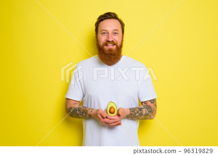 Happy man with beard and tattoos holds an avocado Happy man with beard and tattoos holds an avocado 96319829