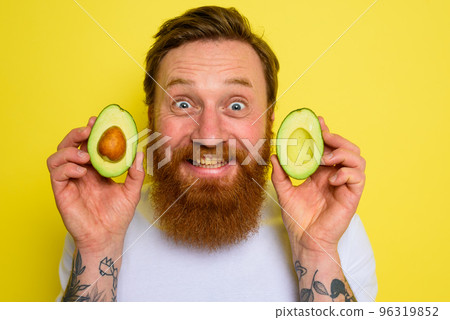 Happy man with beard and tattoos holds an avocado 96319852