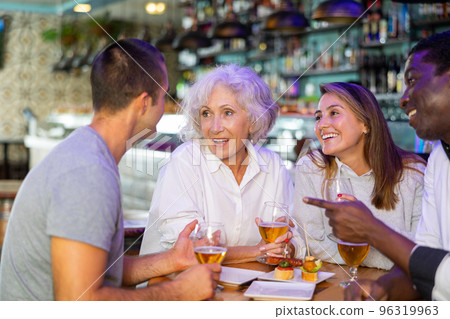Cheerful international friends different ages enjoying pinchos and beer in the evening pub 96319963