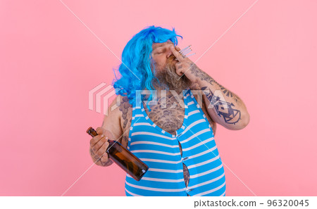 Fat man with beard and wig smokes cigarettes and drinks beer 96320045
