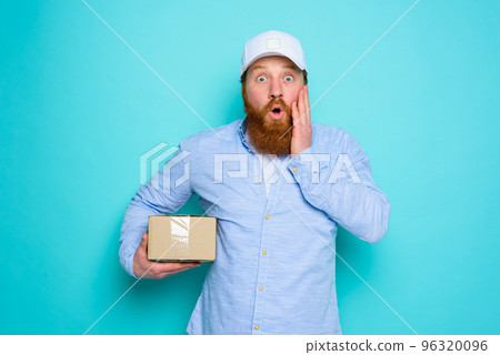 Courier with carton box in hand is surprised about something Courier with carton box in hand is surprised about something 96320096