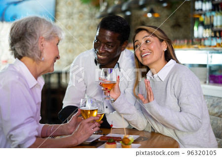 Company of multiracial friends drinking beer and talking with each other during the rest in a pub 96320105