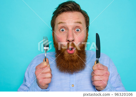 Shocked man with tattoos is ready to eat something with cutlery in hand 96320106