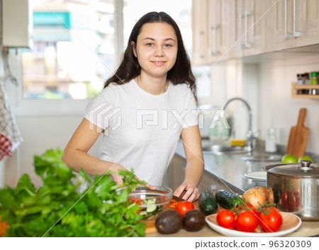 Young woman chopping vegetables at home kitchen Young woman chopping vegetables at home kitchen 96320309