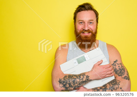 Happy man with beard and tattoos holds an electronic balance 96320576