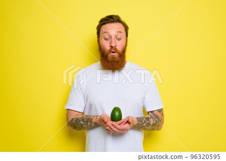 Amazed with beard and tattoos holds an avocado 96320595
