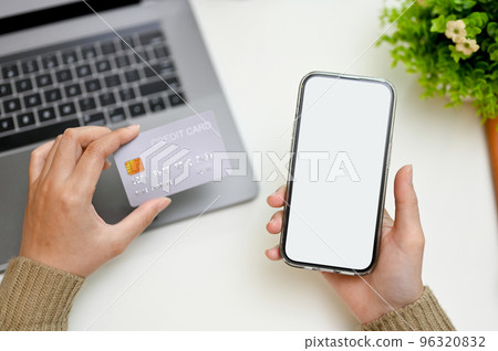 Overhead, Female hands holding her smartphone and credit card over her modern working desk Overhead, Female hands holding her smartphone and credit card over her modern working desk 96320832