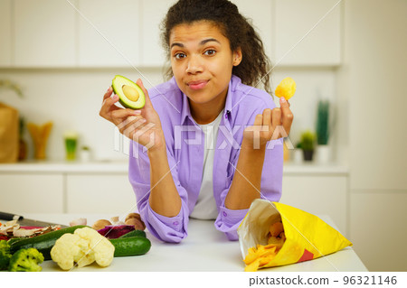 Young cook in the kitchen is confused to eat avocado or cheaps Young cook in the kitchen is confused to eat avocado or cheaps 96321146