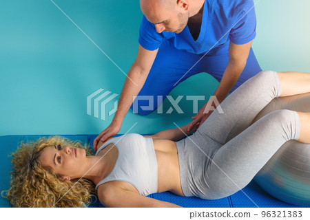 Girl performs exercises with a physiotherapist. Cyan background Girl performs exercises with a physiotherapist. Cyan background 96321383