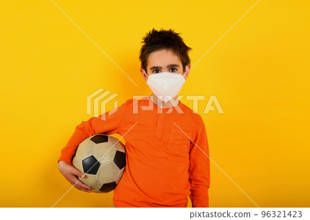 Child wants with face mask for covid-19 coronavirus wants to play at soccer. yellow background 96321423