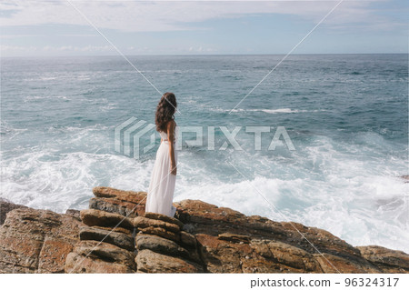Aerial drone view of bride in an amazing dress standing on a cliff and looking at the sea Aerial drone view of bride in an amazing dress standing on a cliff and looking at the sea 96324317