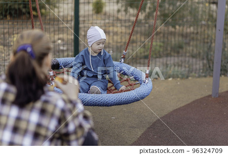 Cute Little boy with down syndrome in a funny hat with his mother, swinging on a swing, soap bubbles Cute Little boy with down syndrome in a funny hat with his mother, swinging on a swing, soap bubbles 96324709
