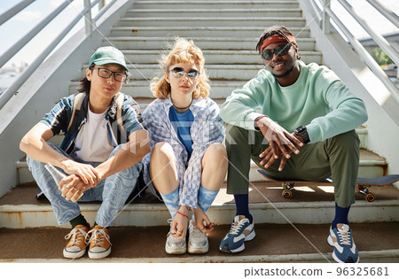 Young people wearing street style clothes outdoors while sitting on stairs 96325681