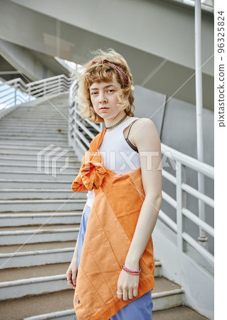 Young woman with curly hair looking at camera in urban city setting 96325824
